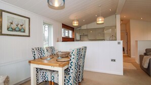 Un comedor con una mesa de madera y sillas estampadas, una cocina al fondo y una obra de arte enmarcada en la pared.