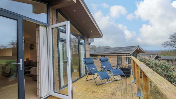 Terraza de madera con dos sillas reclinables y un ventanal que da a una habitación.