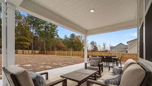 Un patio couvert, aménagé avec du mobilier d’extérieur, une table et offrant une vue sur un jardin avec une clôture en bois et des arbres.