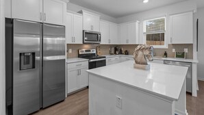 Une cuisine moderne avec des meubles blancs, des appareils en acier inoxydable et un îlot central.