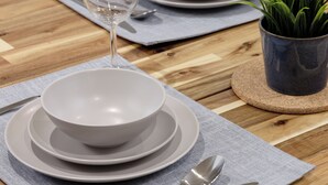 Mesa de jantar posta com pratos brancos, tigelas, talheres e um copo d'água.