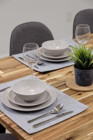 A dining table set with white plates, bowls, cutlery, and a glass of water. - “Bright, cozy 2‑bedroom basement suite in a quiet, family‑friendly area. Near Langley Events Centre and close to Willoughby Town Centre, Willowbrook, Costco, Walmart, cafés, parks, and Hwy 1 for easy travel across the Lower Mainland. (Langley Township)