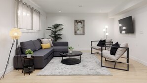 Uma sala de estar moderna com um sofá seccional cinza, uma mesa de centro redonda, um abajur e uma cadeira minimalista.