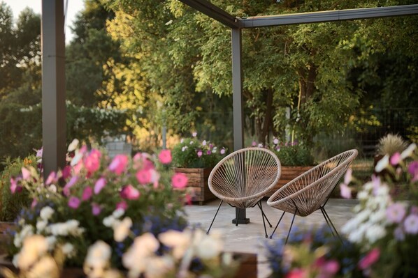 Two wicker chairs under a pergola with a garden backdrop.