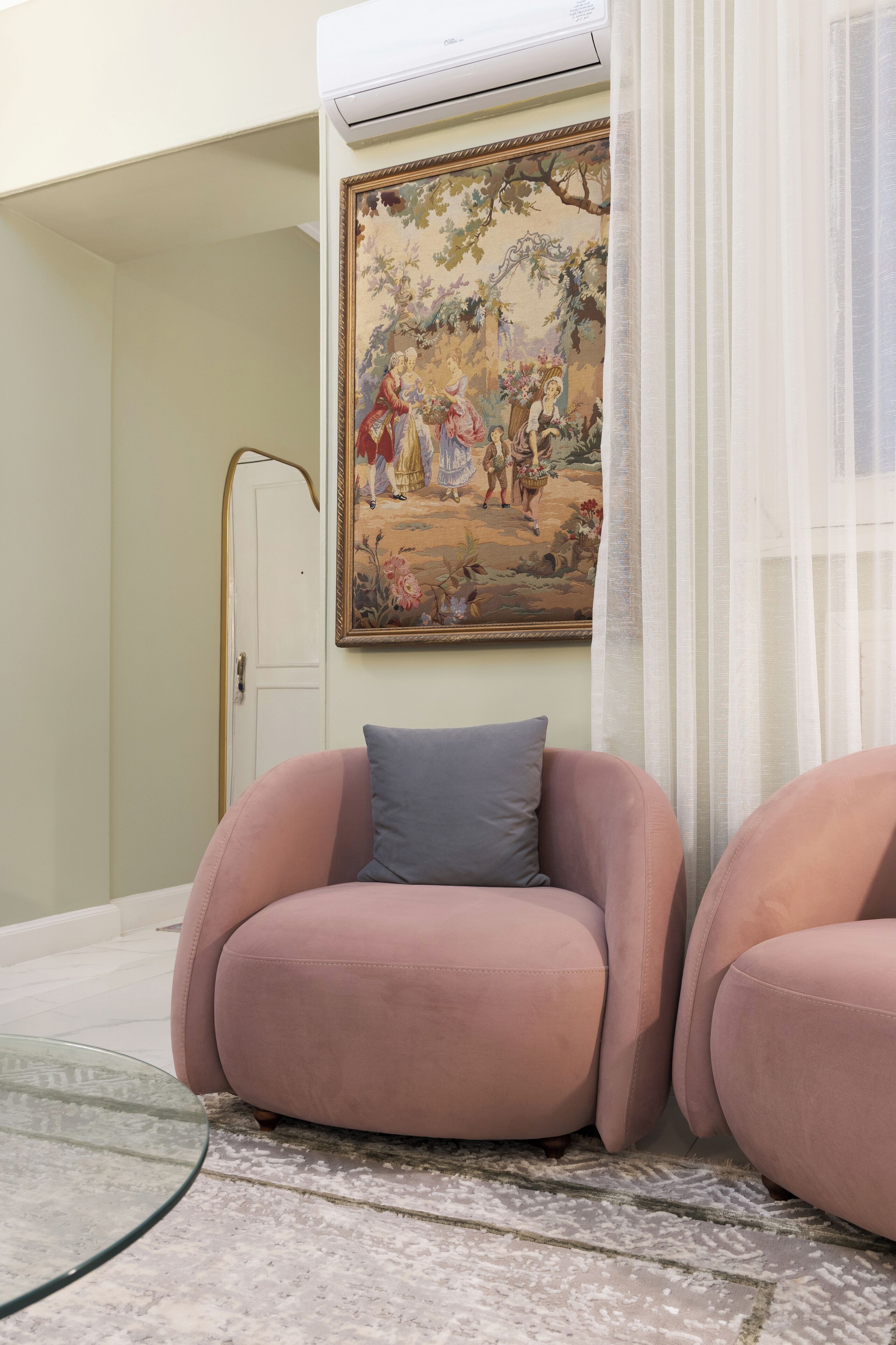 A room with a large floral painting on the wall, a white door, and two pink armchairs with a glass coffee table.
