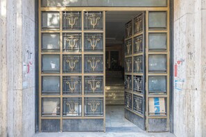 Entrada de un edificio con varios ventanales y puertas de cristal, que dan acceso a una escalera.