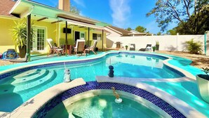 Ein Garten mit Swimmingpool, einer überdachten Terrasse und einem Haus mit gelber Fassade.