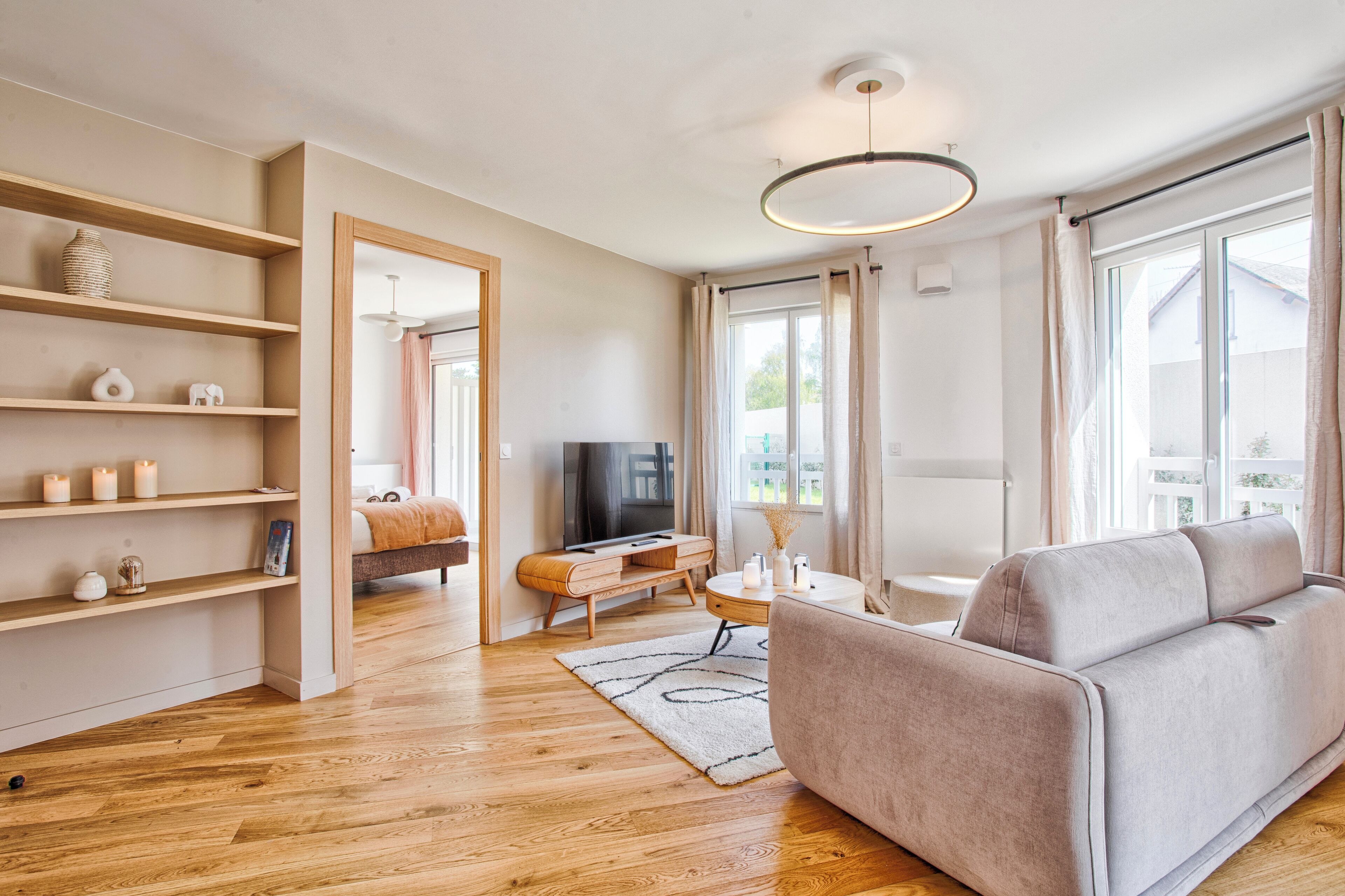 Un salon moderne avec un canapé, un téléviseur, des étagères en bois et une grande fenêtre.
