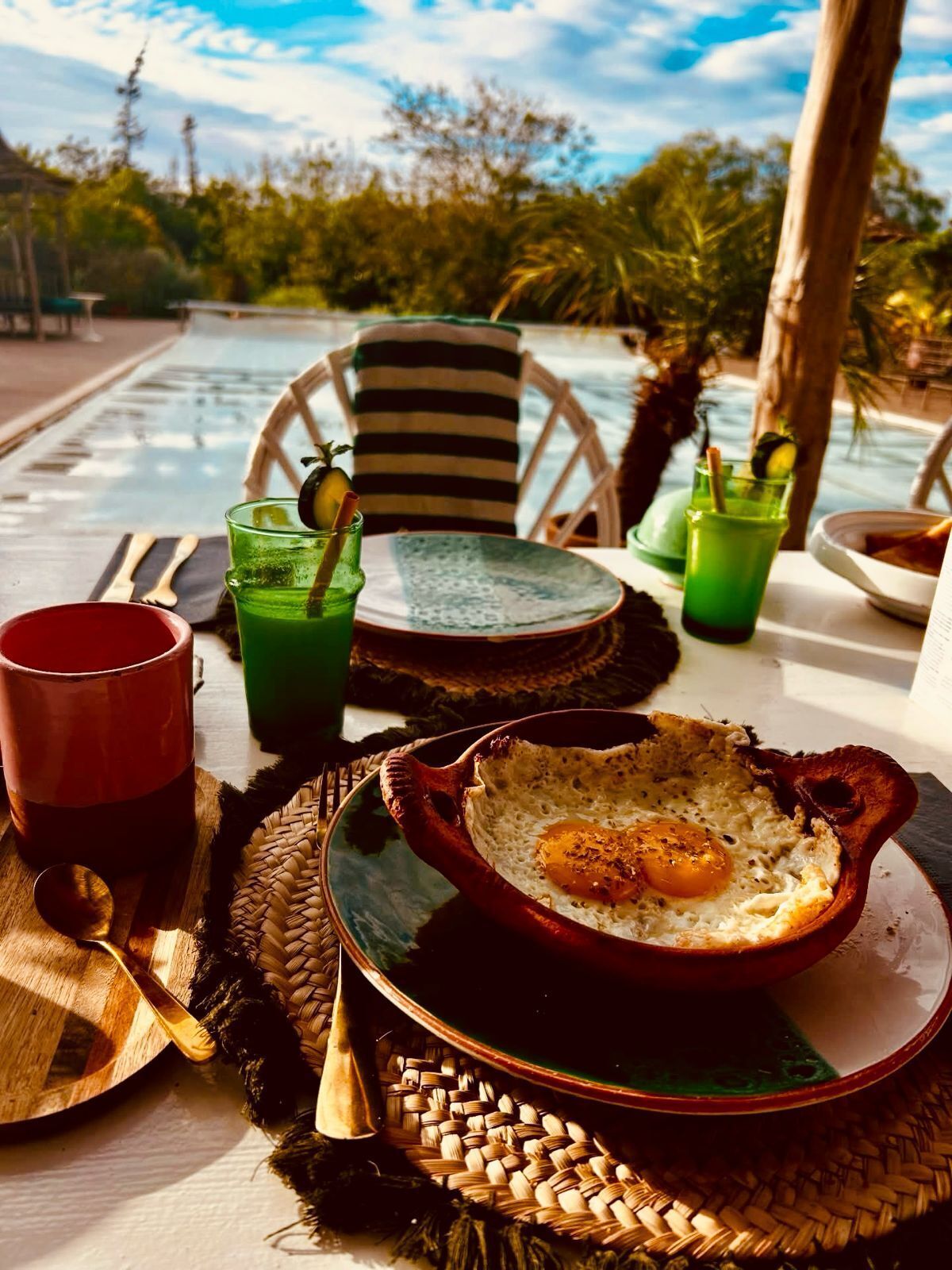 Desayuno con un tazón de huevos, bebidas verdes y una taza roja sobre una mesa con un mantel tejido.