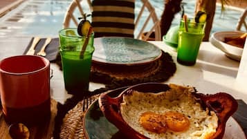 Desayuno con un tazón de huevos, bebidas verdes y una taza roja sobre una mesa con un mantel tejido.