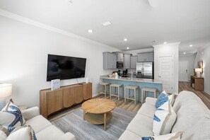 Ein modernes Wohnzimmer mit Flachbildfernseher, Couchtisch aus Holz und einer Couch mit gemusterten Kissen.
