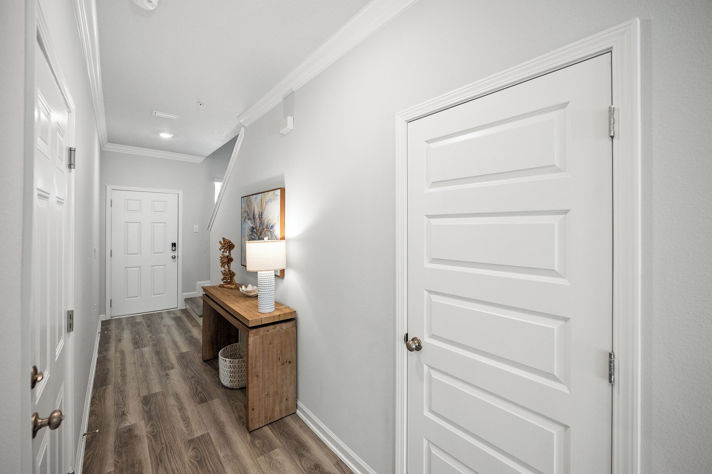 A hallway with a wooden floor, white walls, and a door on the right.