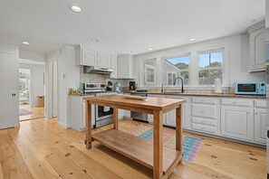 Eine moderne Küche mit weißen Schränken, einem Holztisch und Blick ins Freie durch große Fenster.