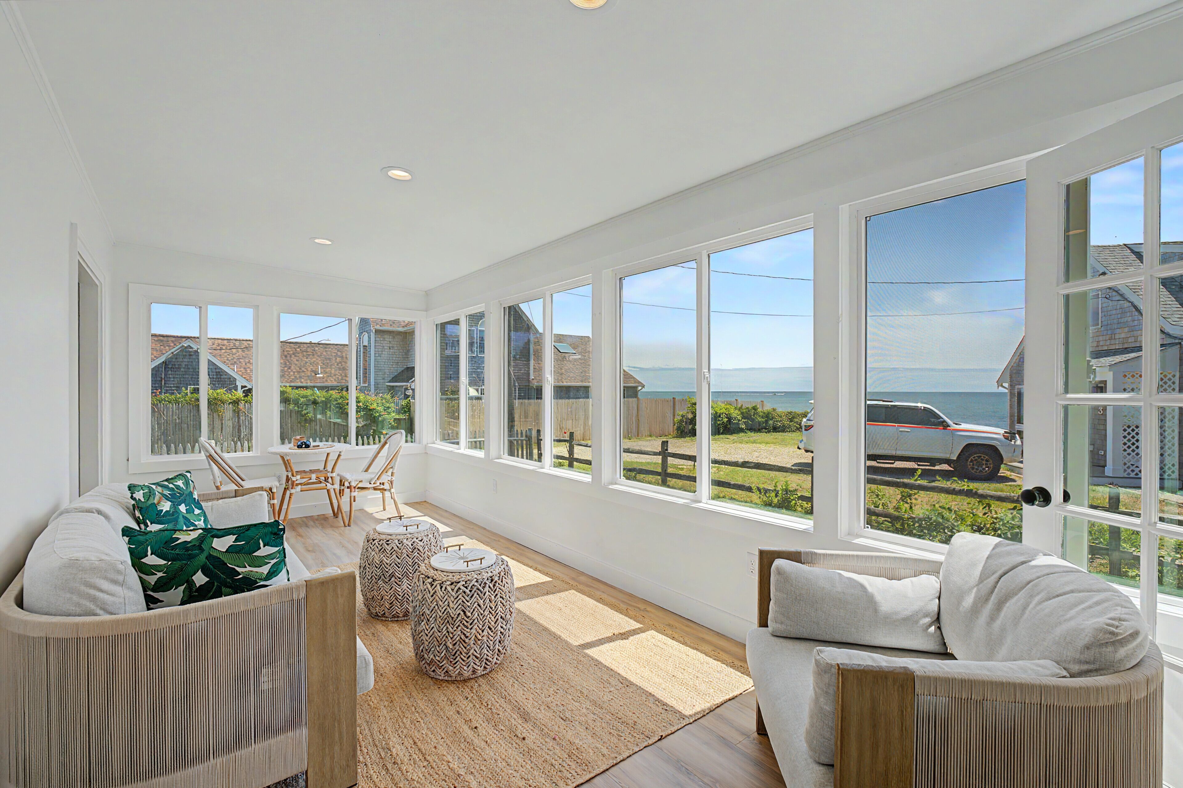 A bright room with large windows, wicker furniture, and a view of the sea.