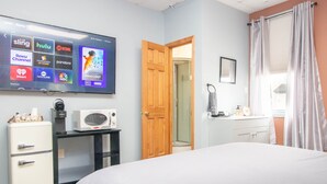 Habitación de hotel con televisión mostrando servicios de streaming, microondas, refrigerador, puerta de madera, baño y cama.