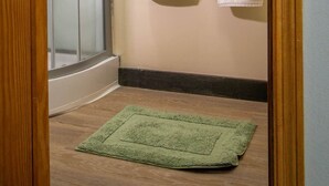 Un baño con mampara de vidrio, un perchero con dos toallas y un tapete verde en el suelo.