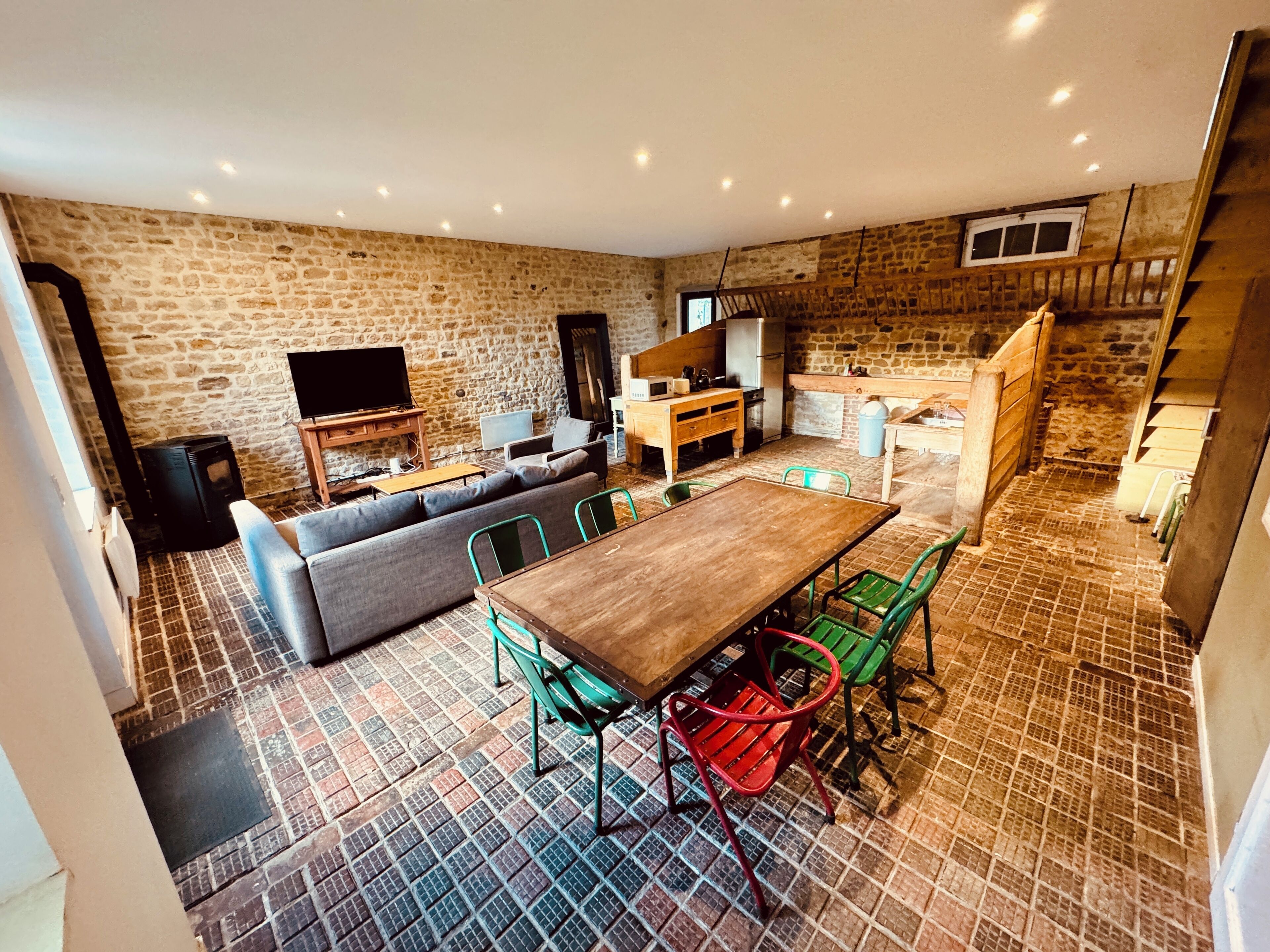 A cozy living room with a stone wall, a wooden dining table, and green chairs.