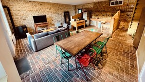 Un salon chaleureux avec un mur en pierre, une table à manger en bois et des chaises vertes.