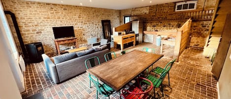 A cozy living room with a stone wall, a wooden dining table, and green chairs.