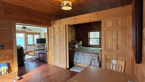 L’intérieur d’un chalet en bois, avec un lit, une table à manger, un téléviseur et une vue sur l’extérieur.