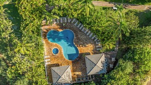 Eine Vogelperspektive zeigt einen luxuriösen Urlaubsort mit einem Schwimmbad, umgeben von üppiger Vegetation und Palmen.