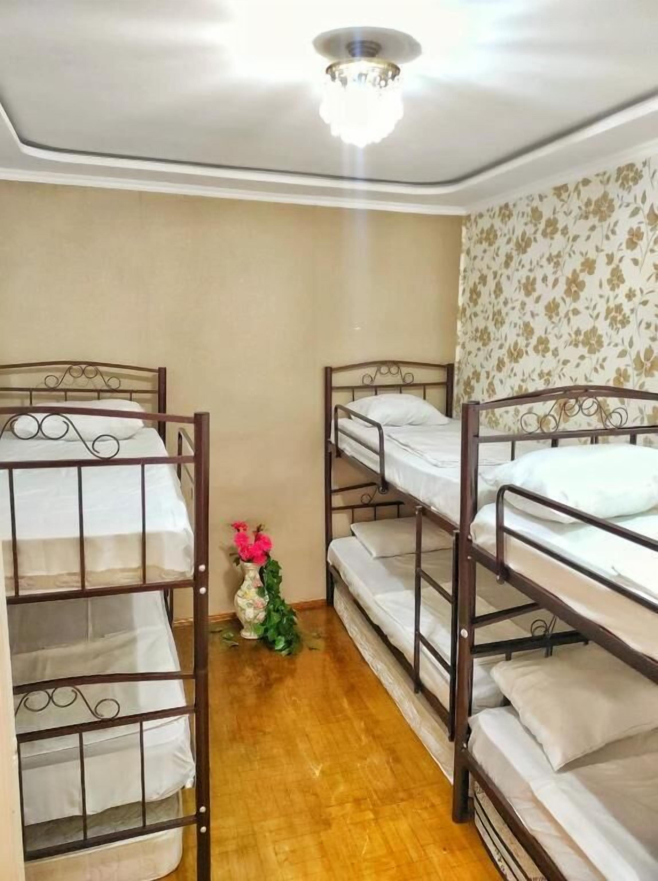Une pièce avec des lits superposés, un plancher en bois, un luminaire au plafond et un papier peint à motifs floraux sur un des murs.