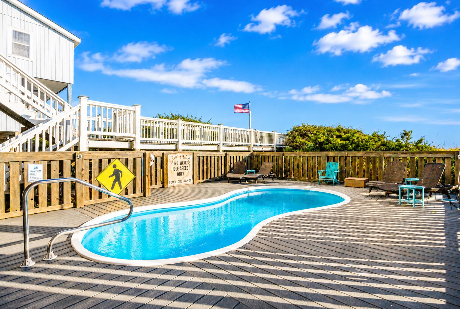 A swimming pool with a wooden deck, lounge chairs, and a flag.