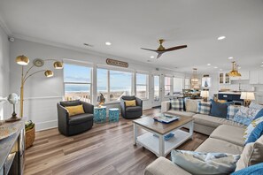 A spacious living room with a view of the beach, a dining area, and a kitchen.