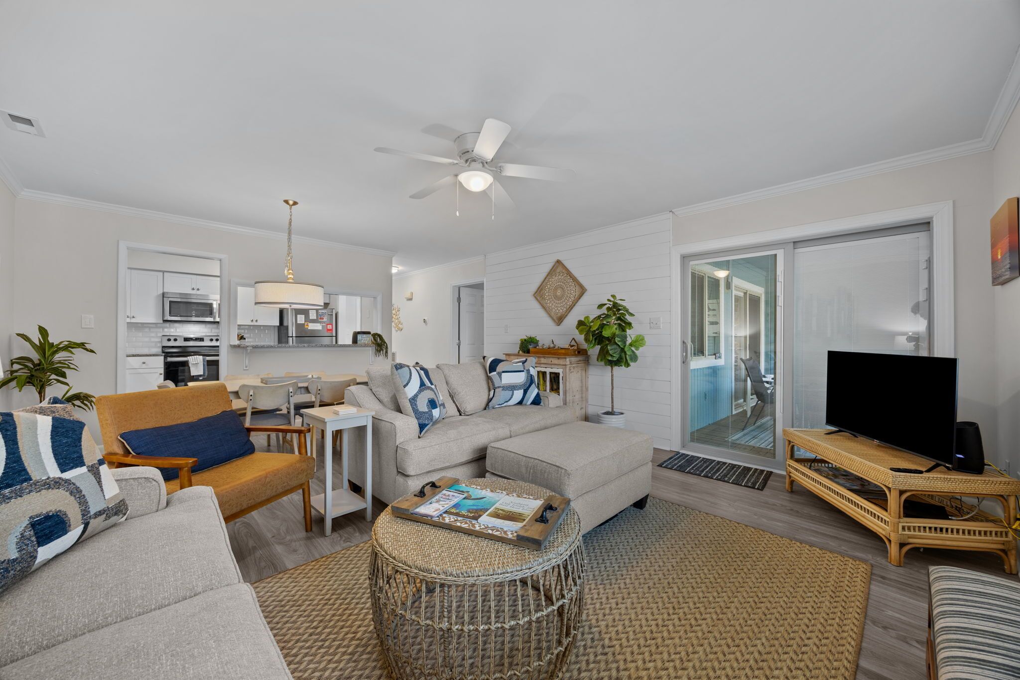A modern living room with a sofa, armchair, and coffee table. There is a television on a stand and a ceiling fan.