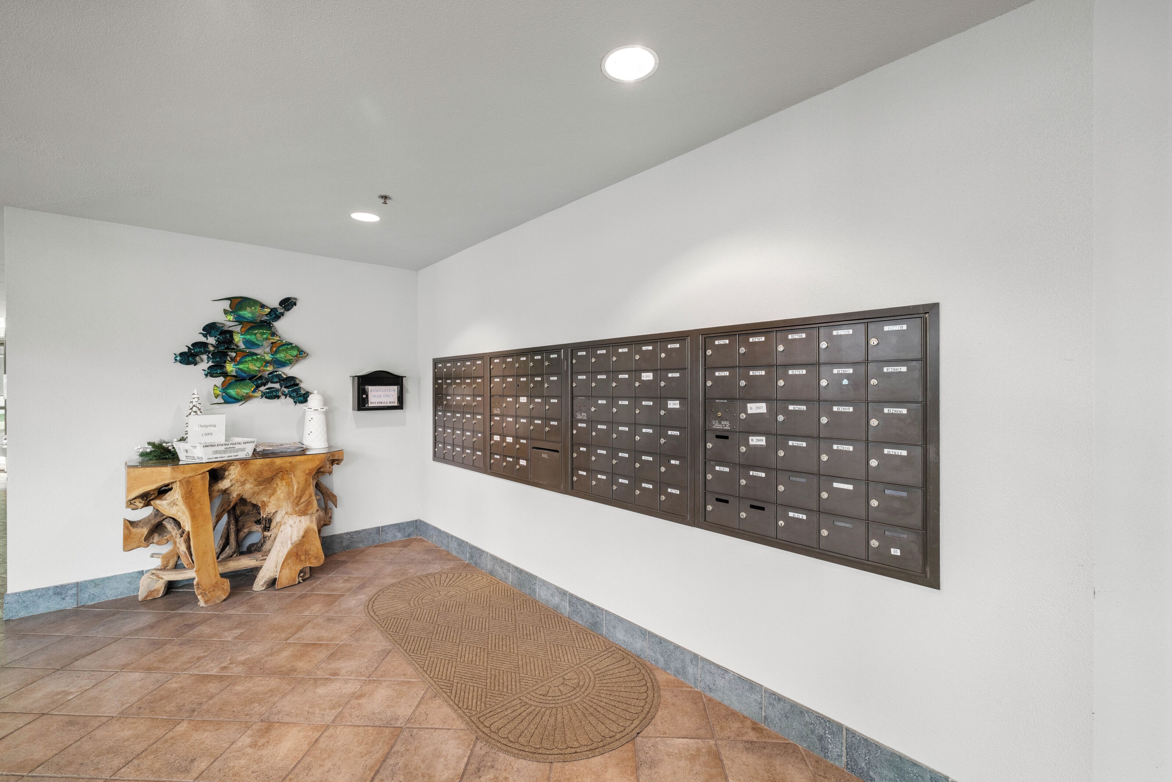 Un espace d’accueil comprenant une console en bois, une boîte aux lettres fixée au mur et un tapis à motifs.
