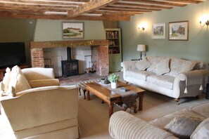 A cozy living room with a fireplace, a sofa, a coffee table, and a bookshelf. - Lovingly restored spacious old pub with a gym and a fire pit in a large garden. (Hindolveston)
