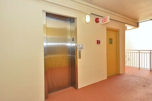 An elevator, an exit sign, and a fire alarm box in a corridor. - Price Drop! Madeira Norte 416🌞Beachfront Condo🐬Private Balcony (Madeira Beach)