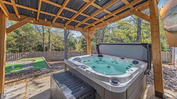 Een hottub onder een houten pergola met uitzicht op een achtertuin en bomen.