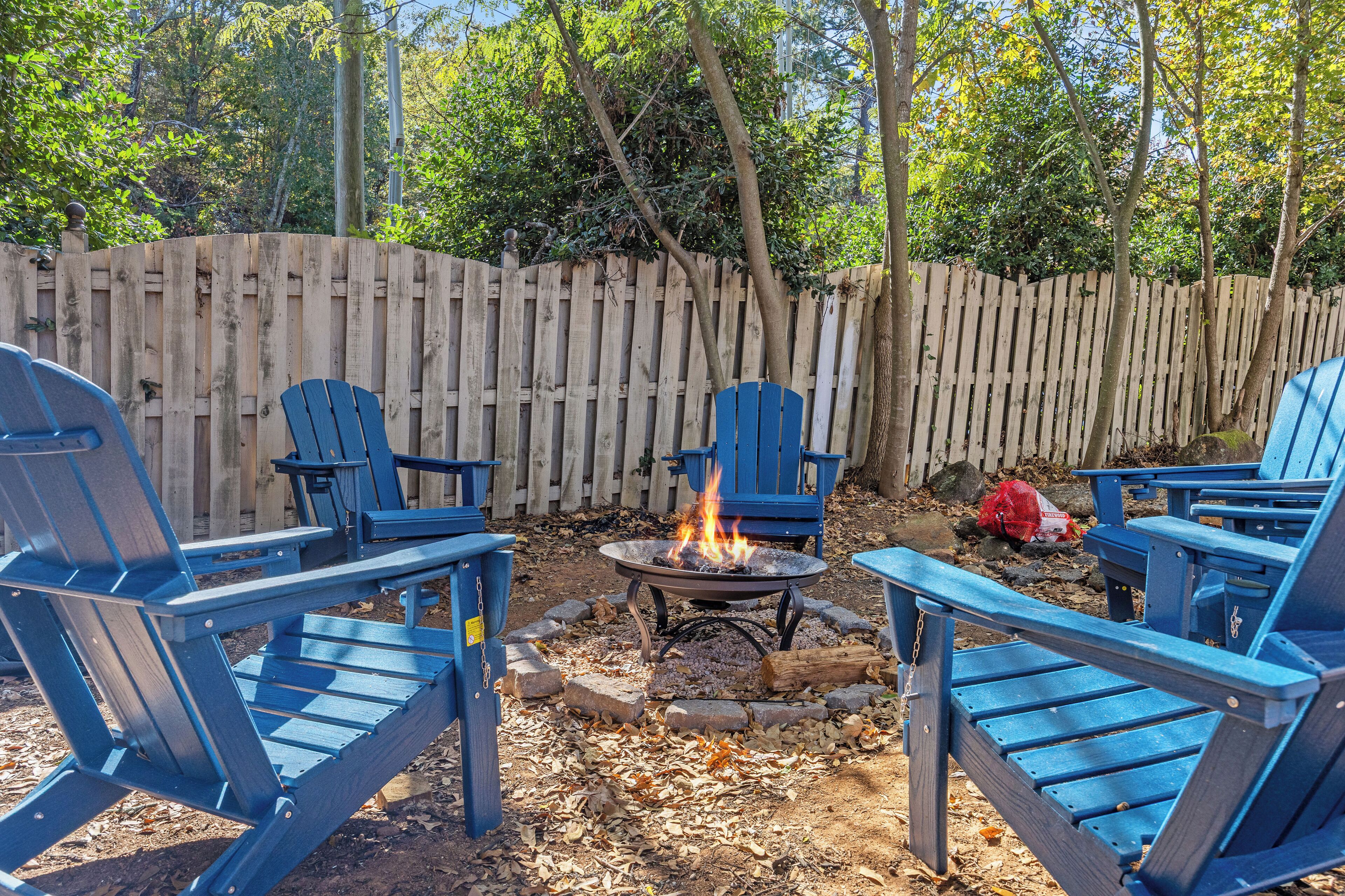 Un patio trasero con cerco de madera, una fogata y sillas Adirondack azules.