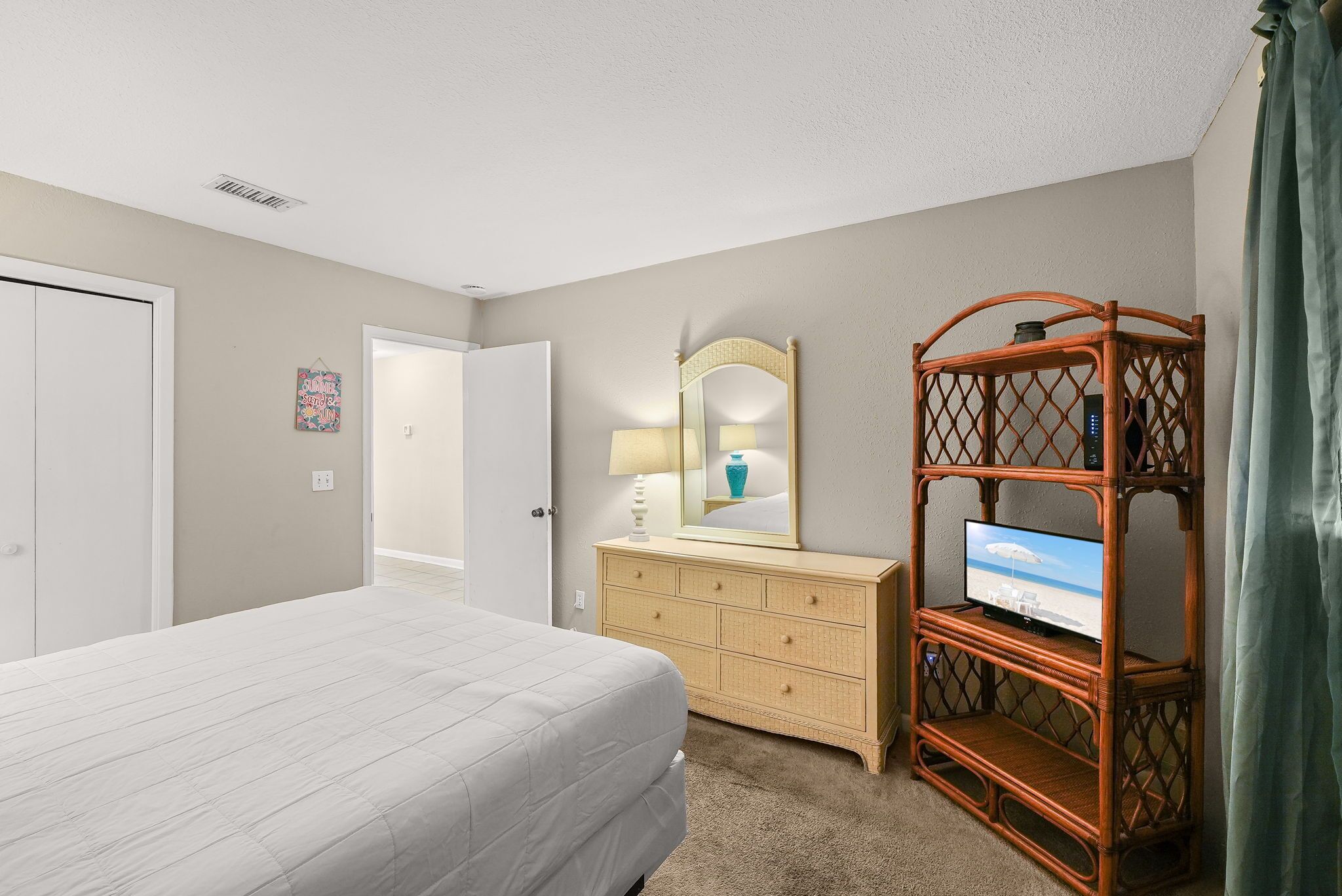 A bedroom with a bed, dresser, mirror, television, and a door.