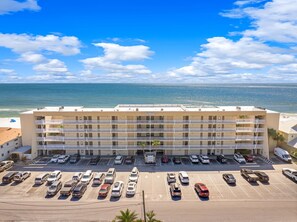 Un h ôtel à plusieurs étages avec un parking situé à l’avant, près d’une plage, avec l’océan en toile de fond.