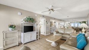 A living room with a TV, sofa, coffee table, and ceiling fan. - Coastal 2BR - pool, beach access & daily tickets (Panama City Beach)