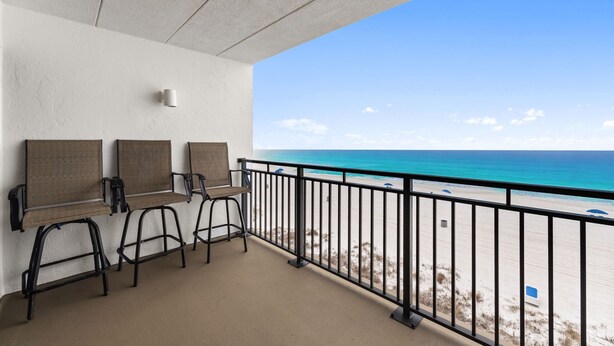 A balcony with a view of the beach, three chairs, and a small table. - Coastal 2BR - pool, beach access & daily tickets (Panama City Beach)