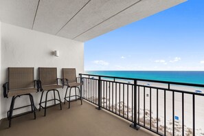Un balcón con vista a la playa, tres sillas y una mesita.