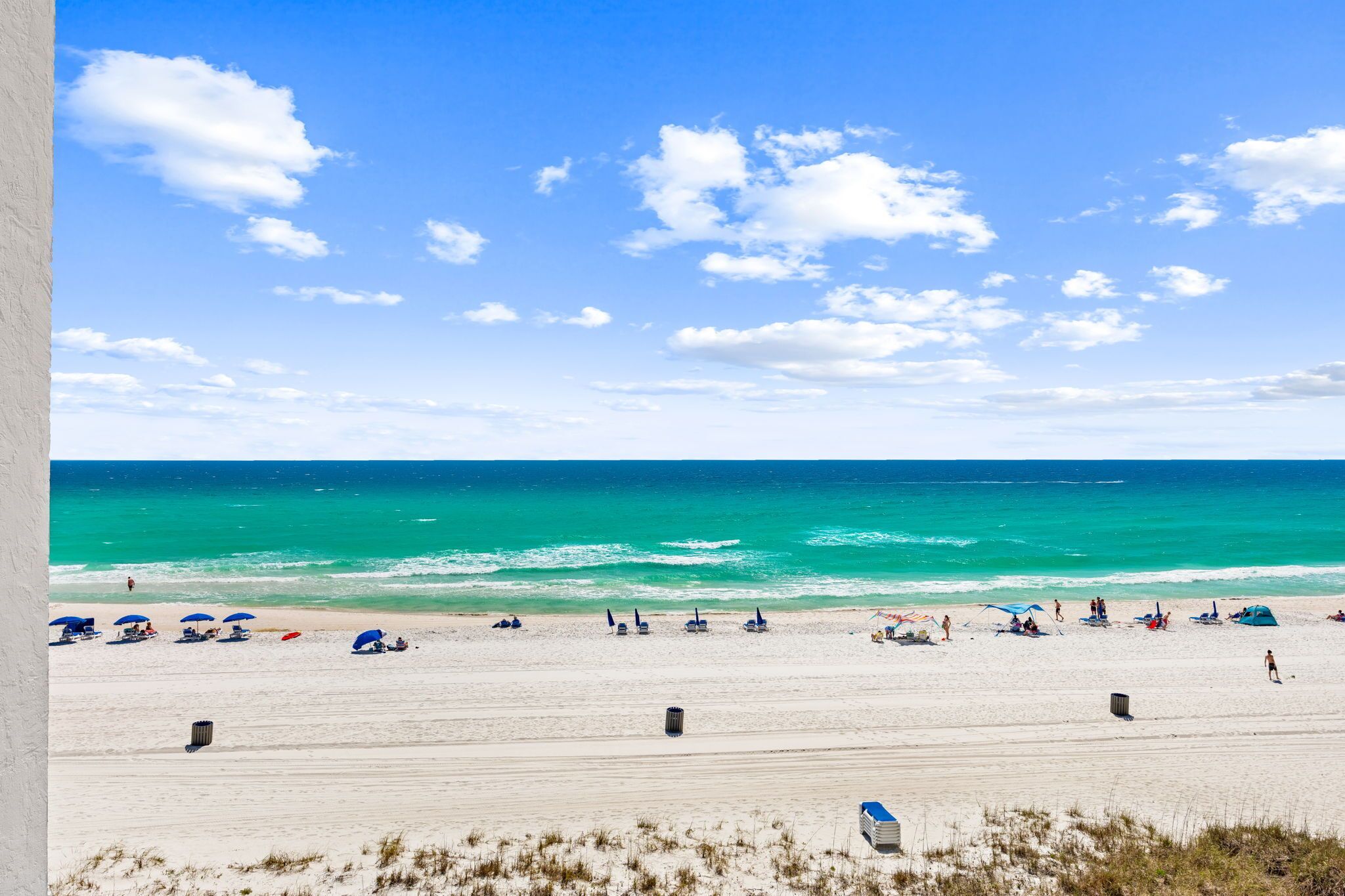 A beach with clear skies, calm waters, and a sandy shore with umbrellas and beach chairs.
