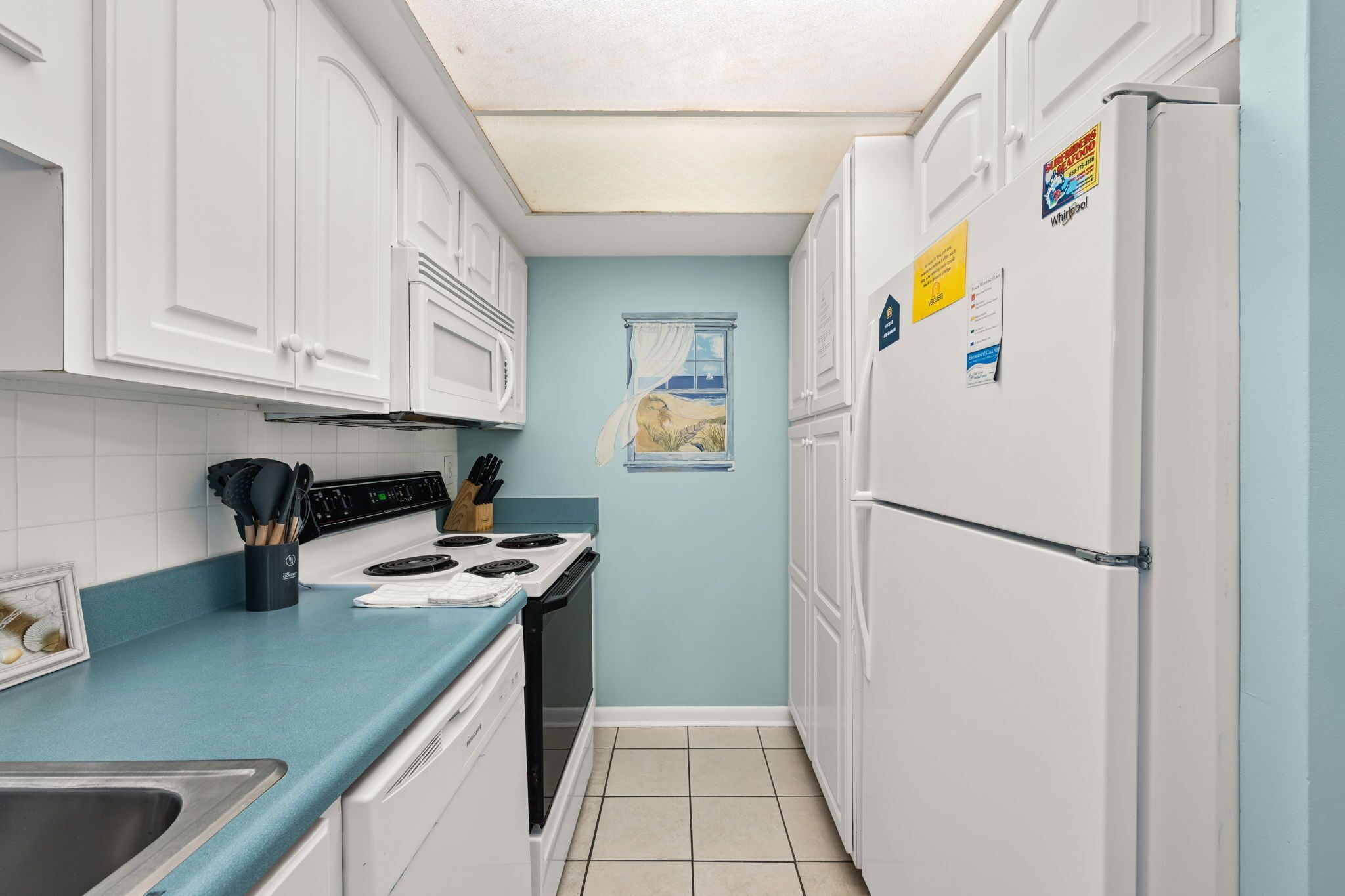 Cocina compacta con armarios blancos, encimera azul, estufa y refrigerador.