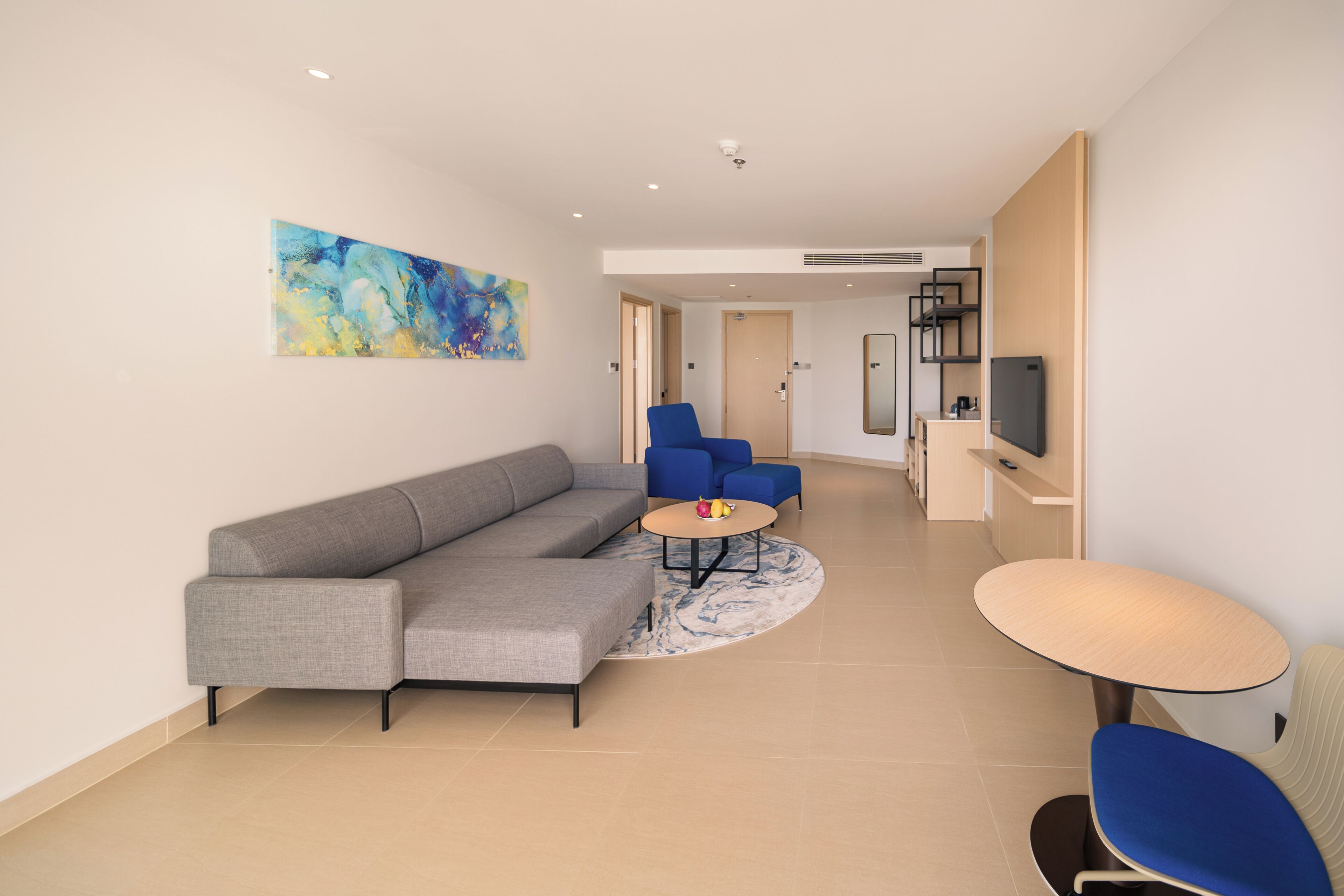 A modern living room with a grey sectional sofa, a blue armchair, a round coffee table, and a small table with a TV.