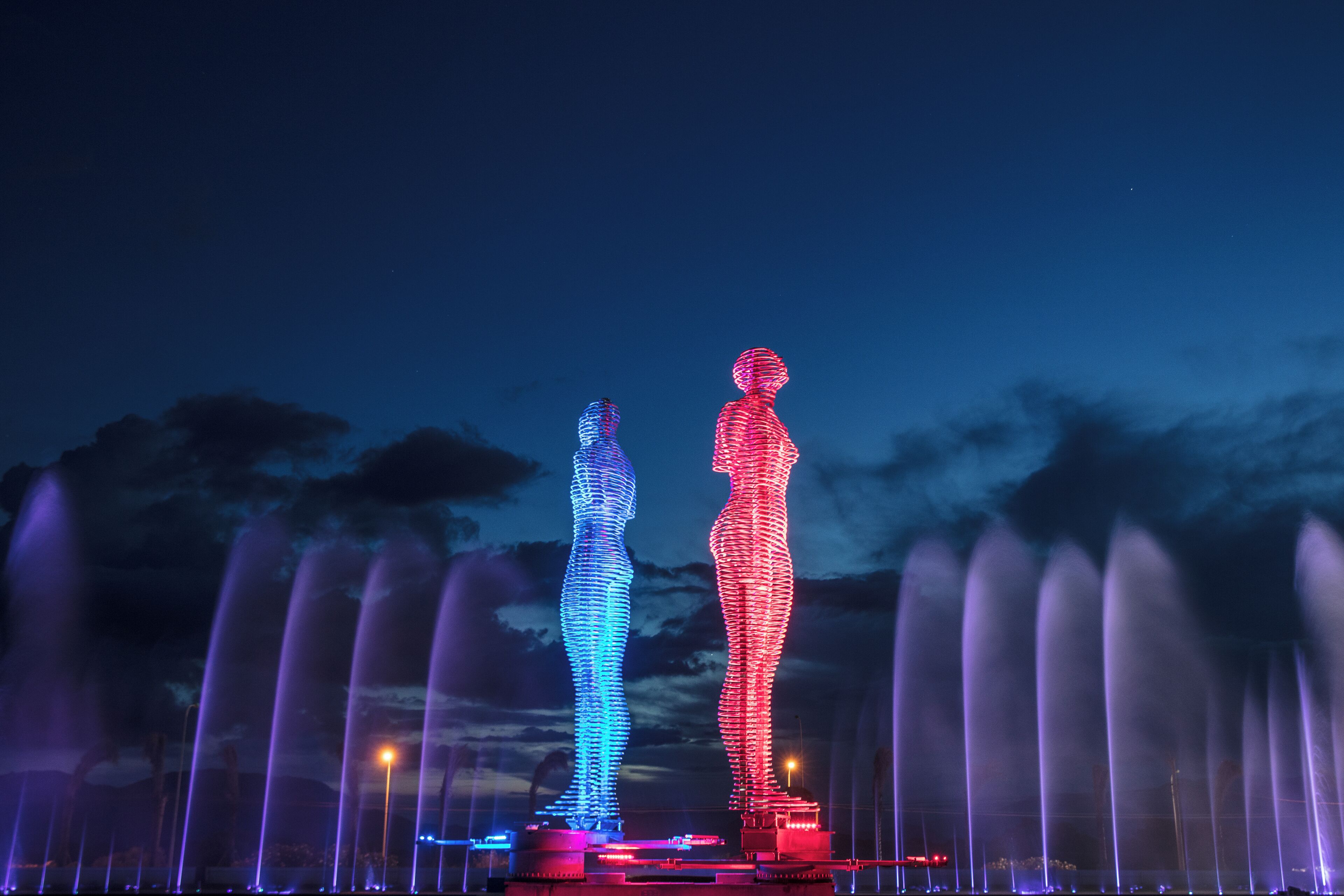 Een nachtelijke scène met twee verlichte figuren en een fonteinshow.