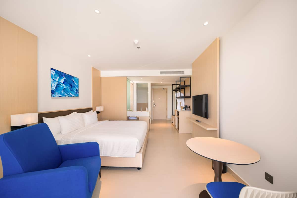 A modern hotel room with a bed, a blue sofa, a small table, and a TV.