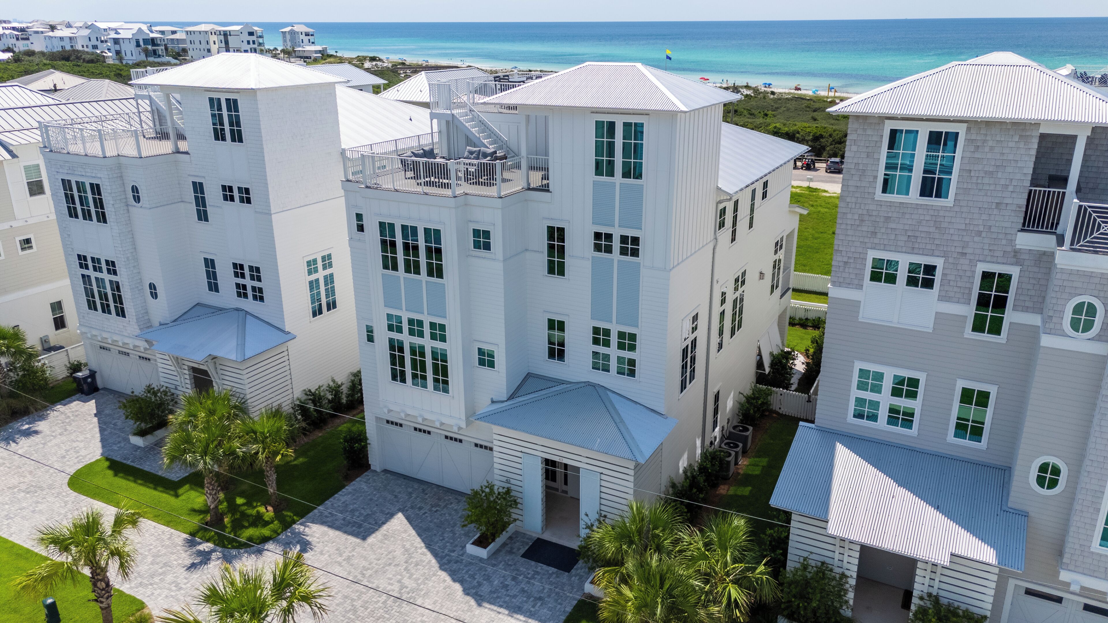 A modern multi-story hotel with a rooftop terrace, a well-maintained lawn, and a view of the ocean.