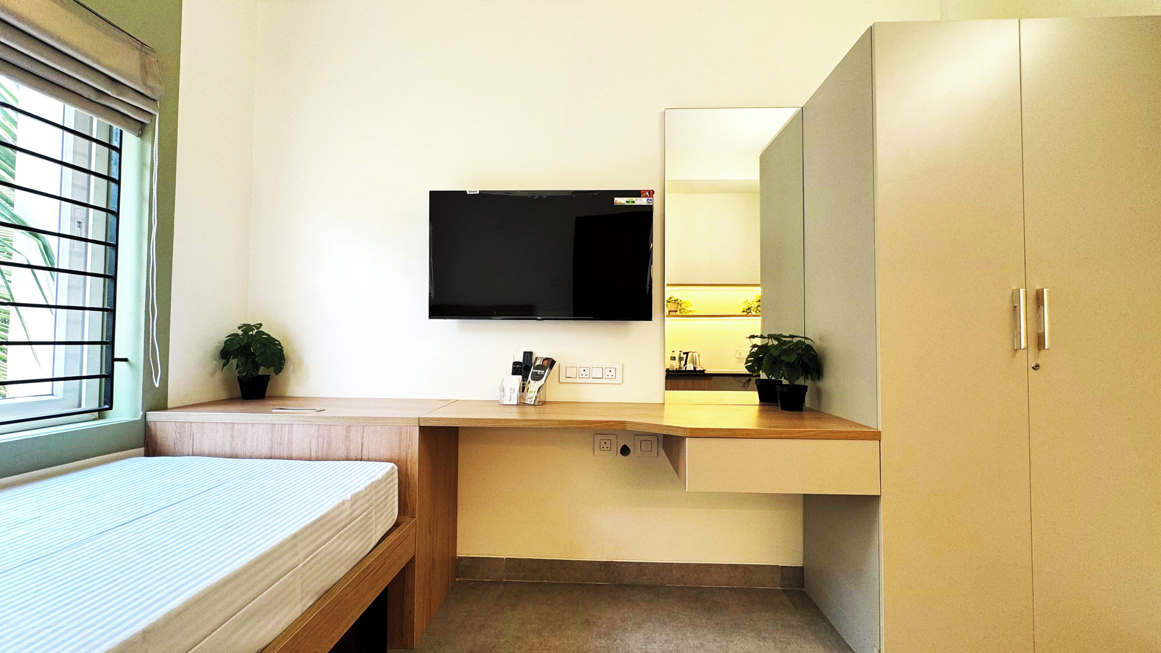 Een kleine kamer met een bed, een bureau met een flatscreen-tv en een kledingkast.