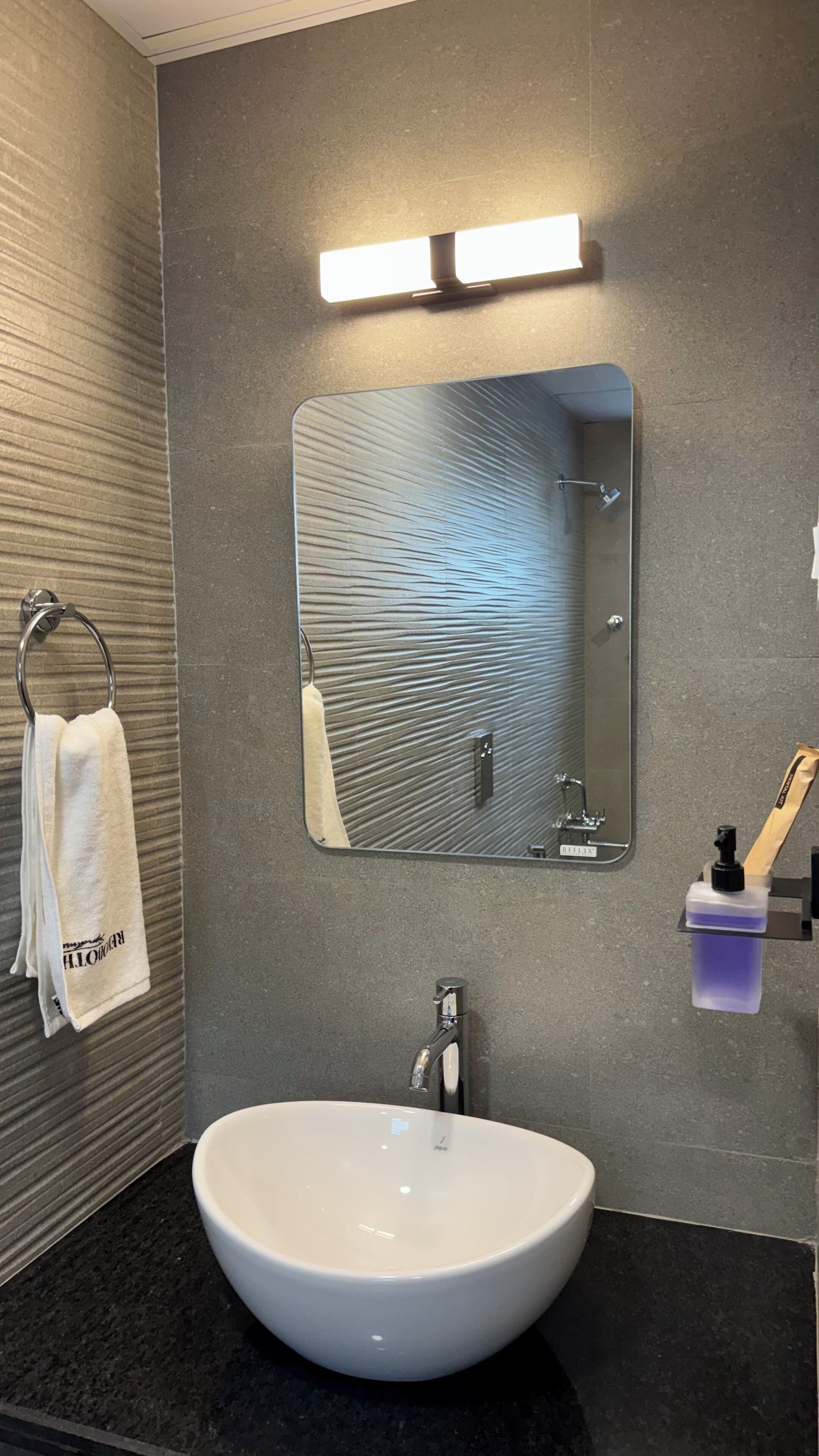 Une salle de bain avec un lavabo rond, un porte-serviettes avec une serviette, un miroir et un distributeur de savon.