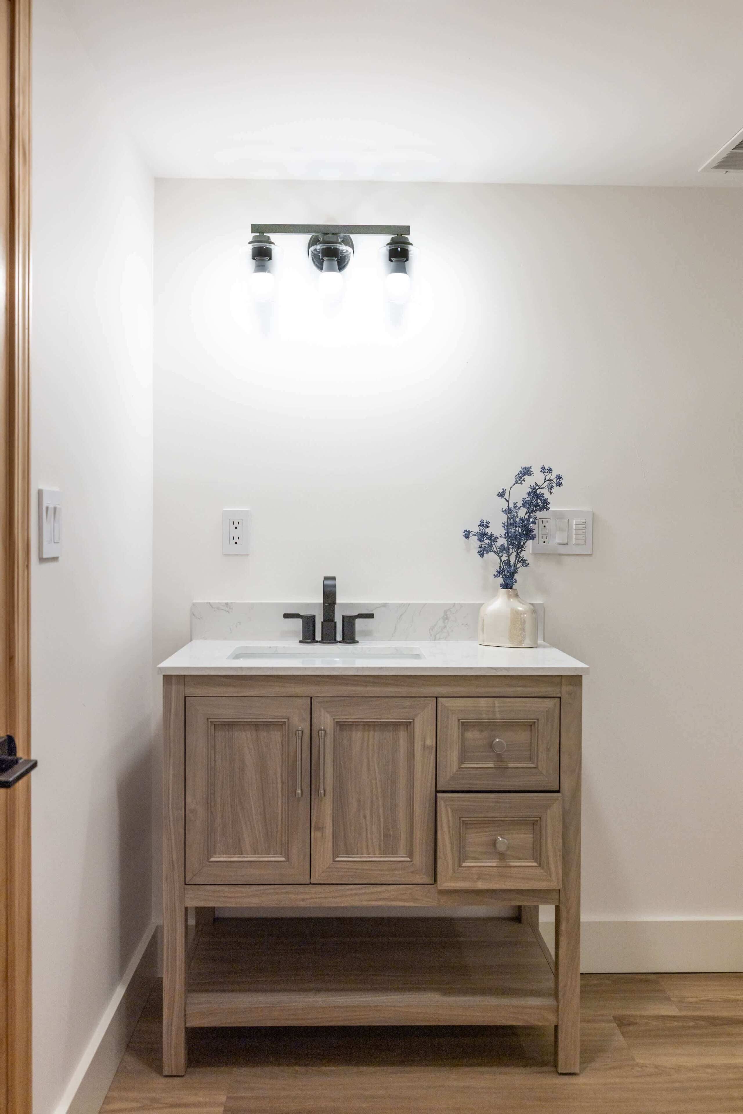 A bathroom with a wooden vanity, a white sink, and a vase with flowers.