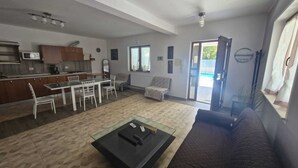Un vaste espace de vie comprenant une table à manger, un canapé et une table basse. On aperçoit une cuisine à l’arrière-plan, avec un four à micro-ondes et des placards.