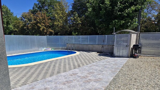 Un jardin avec une piscine, une terrasse dallée et une zone délimitée par une clôture.